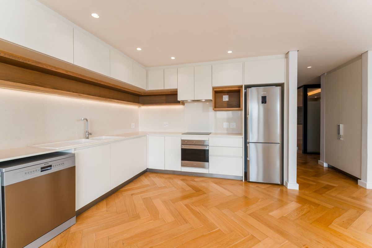 Modern kitchen featuring sleek white cabinetry, stone countertops, integrated appliances, and elegant herringbone timber flooring with warm under-cabinet lighting.