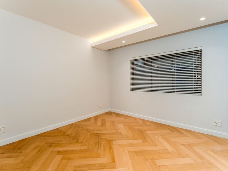 A bright, empty bedroom featuring high-quality herringbone timber flooring, recessed ceiling lighting, and modern venetian blinds.