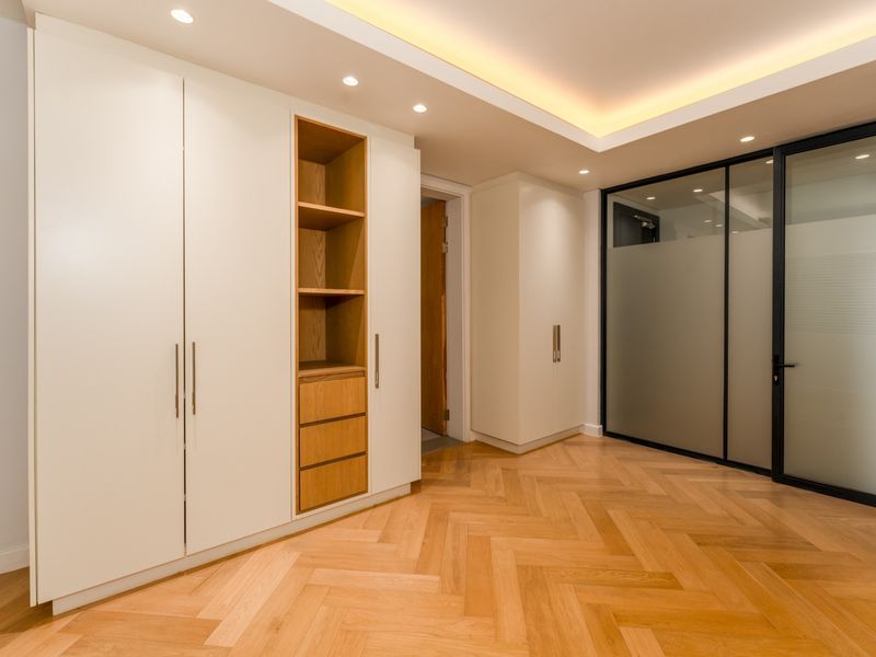 A modern hallway featuring high-quality herringbone timber flooring, extensive built-in cabinetry with integrated shelving, and elegant recessed and cove lighting.