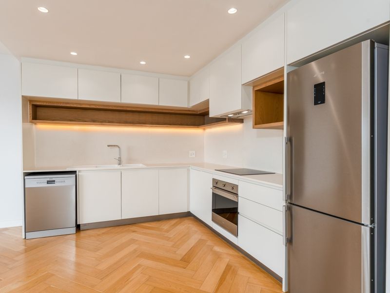 Modern kitchen featuring sleek white cabinetry, herringbone timber flooring, integrated appliances, and warm under-cabinet lighting in a clean, minimalist design.
