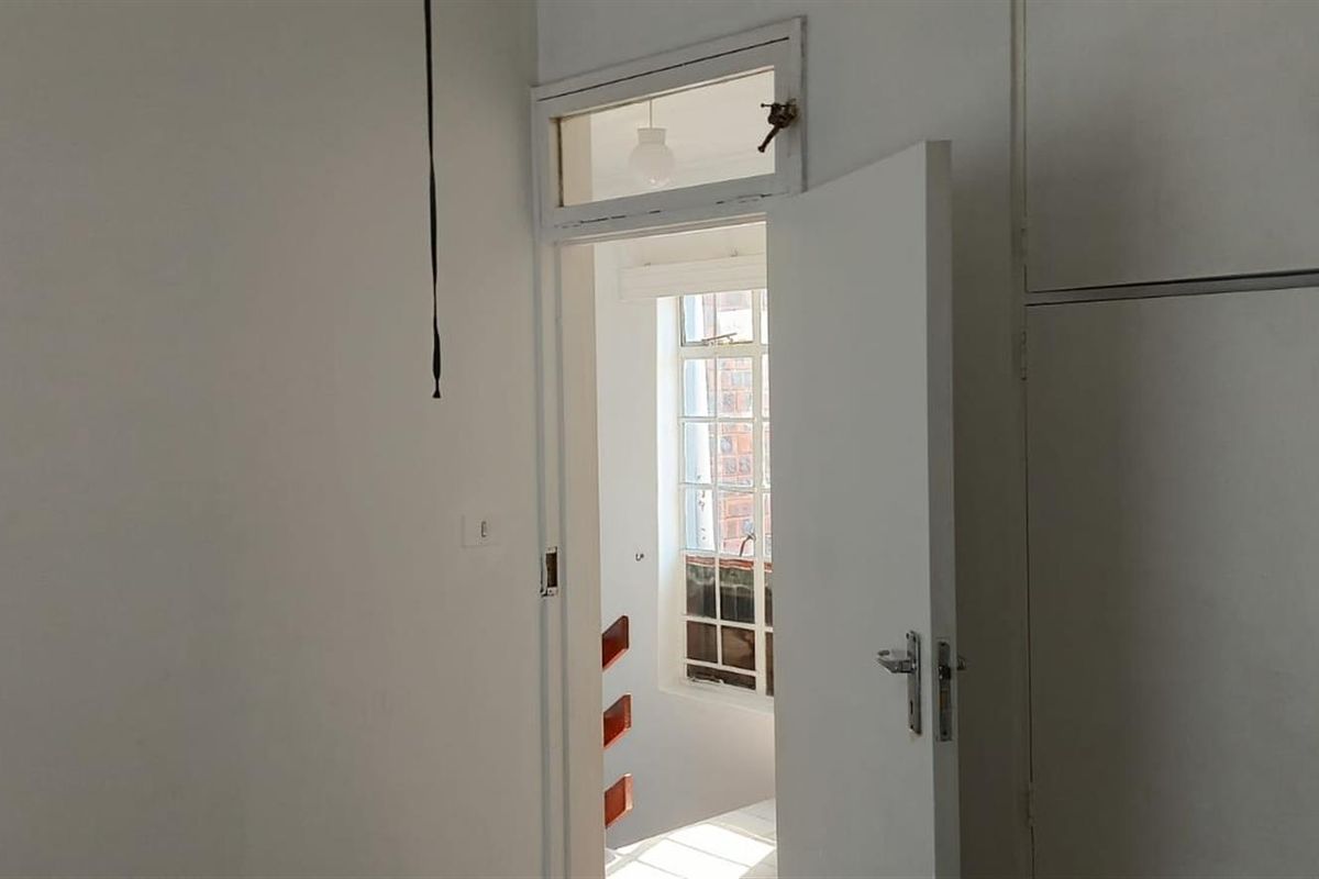 A bedroom interior featuring built-in storage cupboards and a doorway leading to an adjacent space with a window.