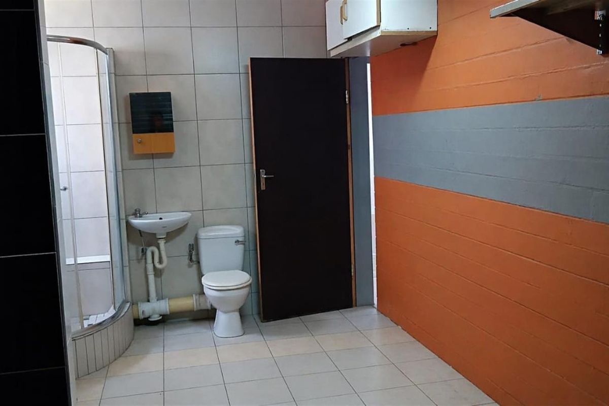 A functional bathroom featuring a corner shower enclosure, pedestal basin, and toilet, with tiled flooring and painted brick wall finishes.