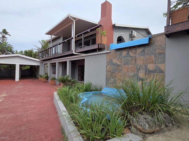 Exterior view of the property featuring a paved driveway, covered carport, balcony, and a small water feature with stone cladding.