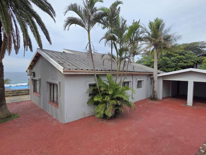 Exterior view of the property featuring a paved driveway, attached carport, and established palm trees with a glimpse of the ocean and pool area.