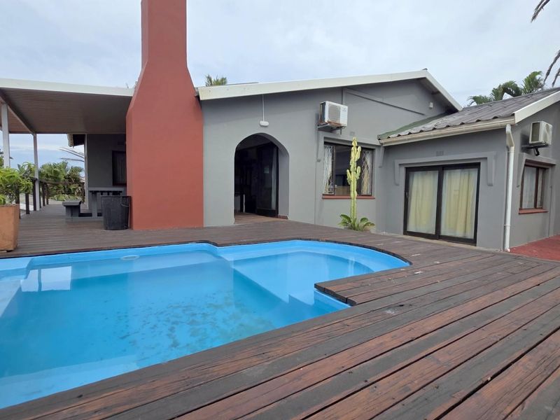 Rear exterior view featuring a swimming pool, timber decking, covered patio area, and a prominent chimney stack.