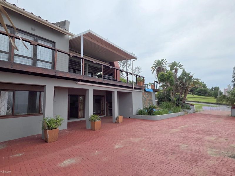 Rear exterior view of a multi-level house featuring a paved courtyard, a covered patio area, and an elevated wooden balcony.