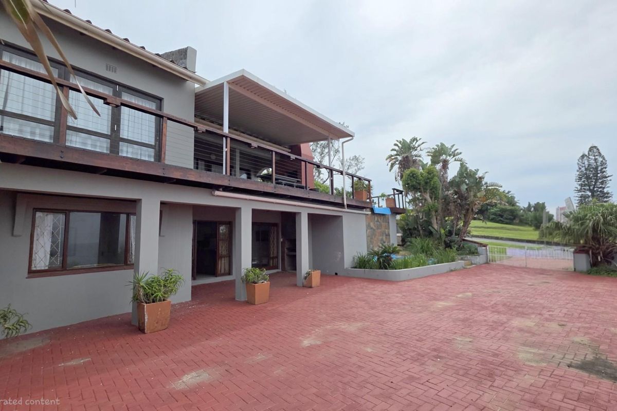 Rear exterior view of a multi-level house featuring a paved courtyard, a covered patio area, and an elevated wooden balcony.