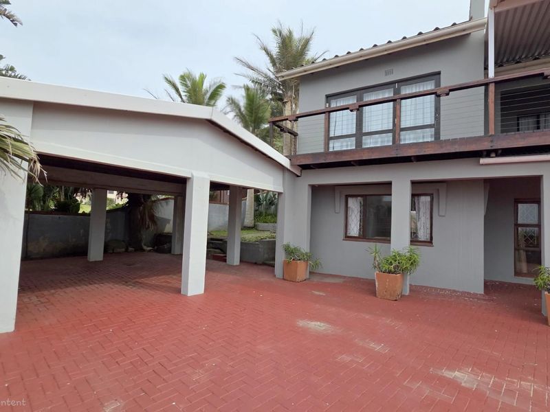 Exterior view of the property featuring a covered carport, paved driveway, and an upper-level balcony with timber railings.