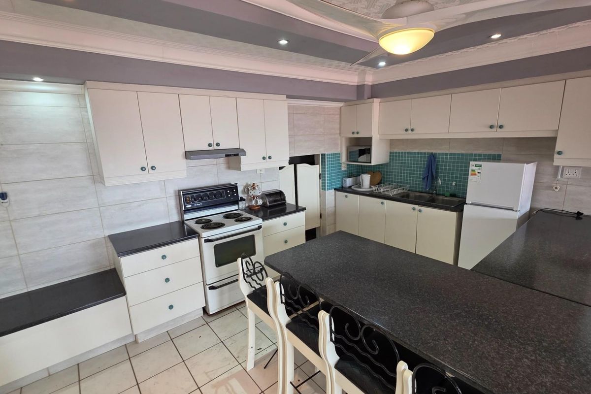 A functional kitchen featuring white cabinetry, dark granite countertops, a built-in stove with extractor fan, and a central breakfast island.