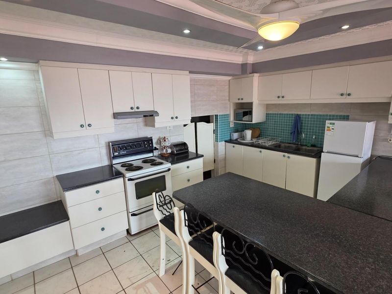 A functional kitchen featuring white cabinetry, dark granite countertops, a built-in stove with extractor fan, and a central breakfast island.