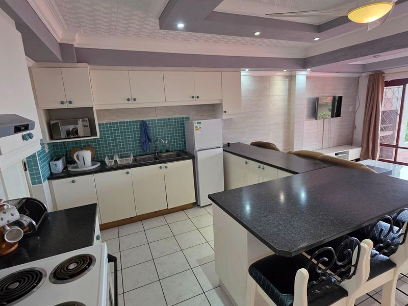 Open-plan kitchen featuring a breakfast bar, tiled flooring, built-in cabinetry, and integrated stove, flowing into the adjacent living area with patio access.