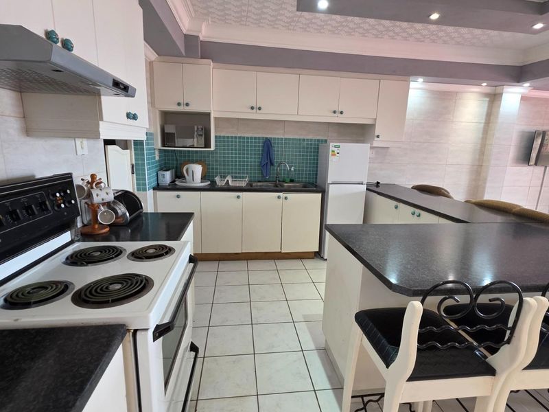 Open-plan kitchen featuring a breakfast bar, tiled flooring, built-in cabinetry, and a freestanding electric stove with an extractor fan.