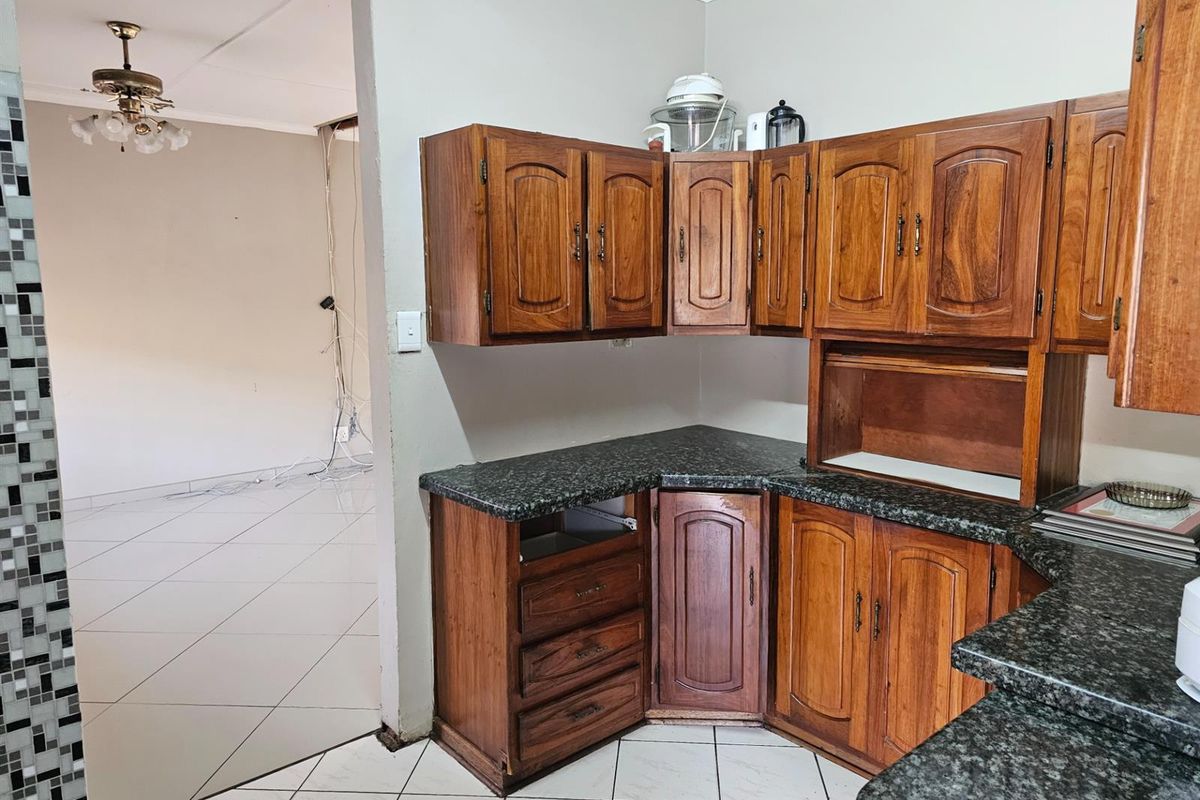 A dated kitchen featuring traditional timber cabinetry and granite-look countertops, adjacent to an open-plan living area requiring ceiling and electrical repairs.