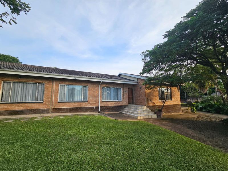 A classic single-story brick house featuring a tiled roof, front entrance steps, and a spacious front lawn with established trees.