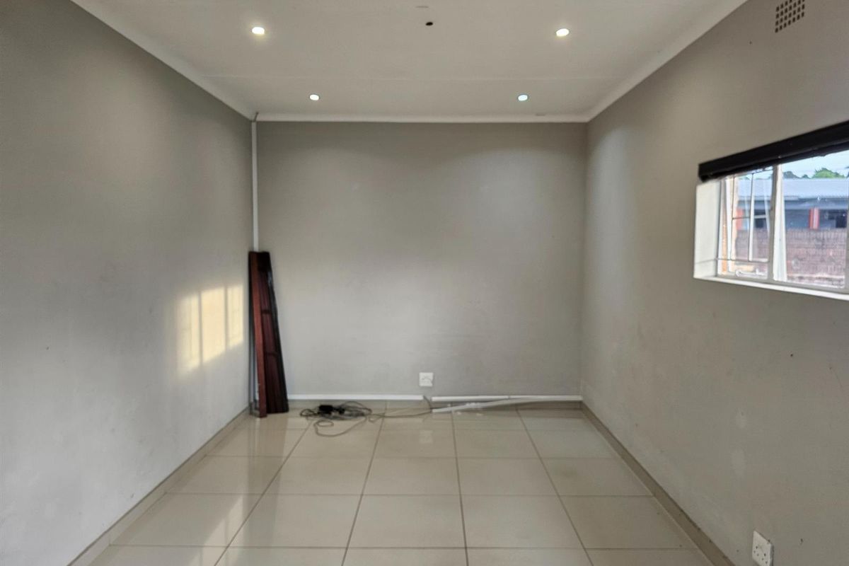 An empty, neutral-toned room featuring tiled flooring, recessed ceiling lighting, and a window with a roller blind.