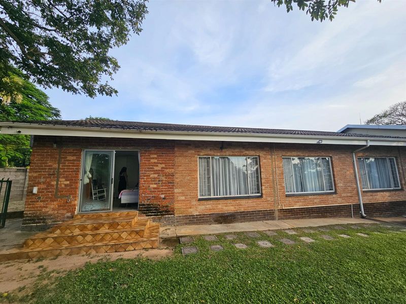 Rear view of a single-story brick house featuring large windows, a tiled entrance step, and a surrounding lawn area.