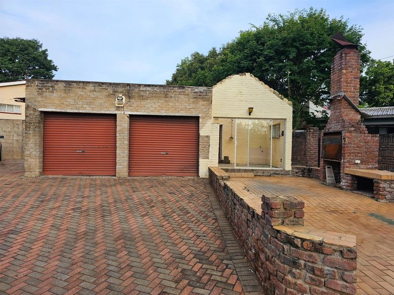 Exterior view featuring a double garage with roller doors, an adjacent patio area with a built-in brick fireplace, and paved driveway.
