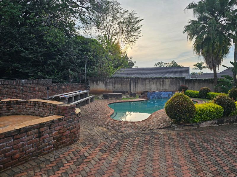 Outdoor pool area featuring a paved patio, brick-built seating, and a swimming pool set against a landscaped garden backdrop.