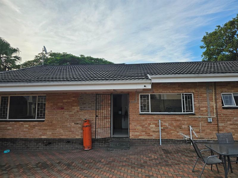 Rear exterior view of a brick-faced house featuring a tiled roof, security gates, and a paved patio area.