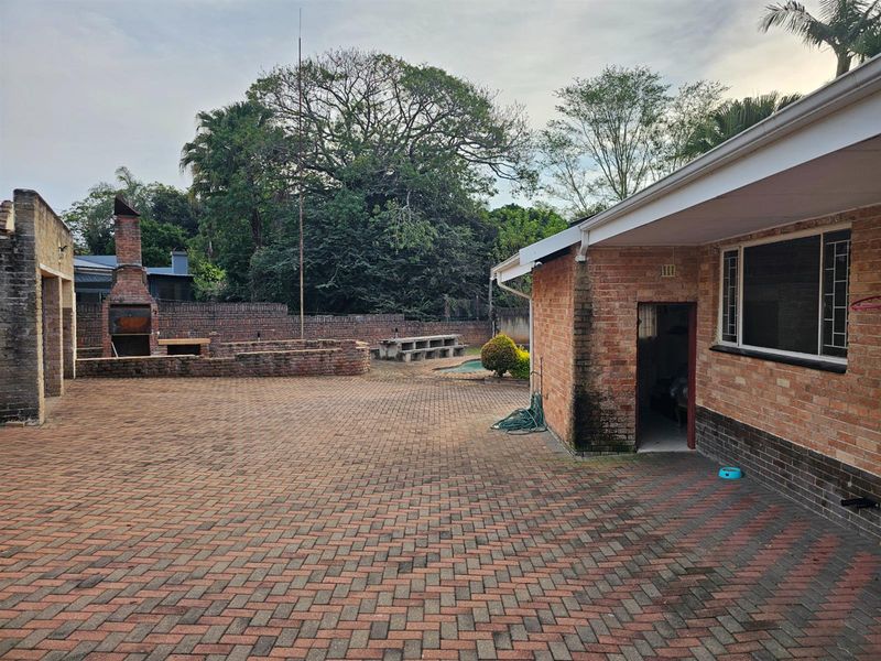 Spacious rear courtyard featuring brick paving, a built-in outdoor fireplace, and direct access to the main dwelling.