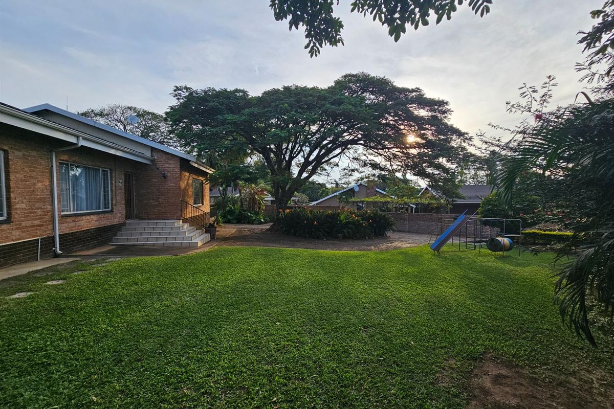Spacious rear garden featuring a well-maintained lawn, mature trees, paved patio area, and direct access to the house via tiled steps.