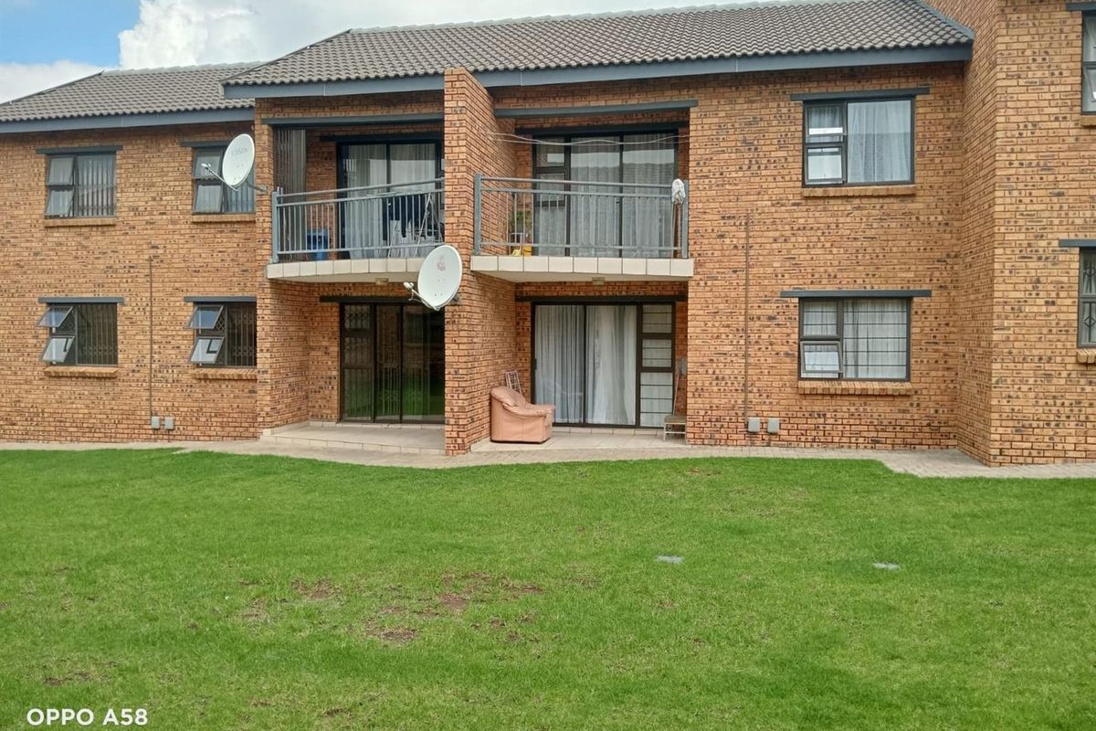 Rear view of a two-story brick apartment building featuring a ground-floor patio and an upper-level balcony with metal railings and sliding glass doors.