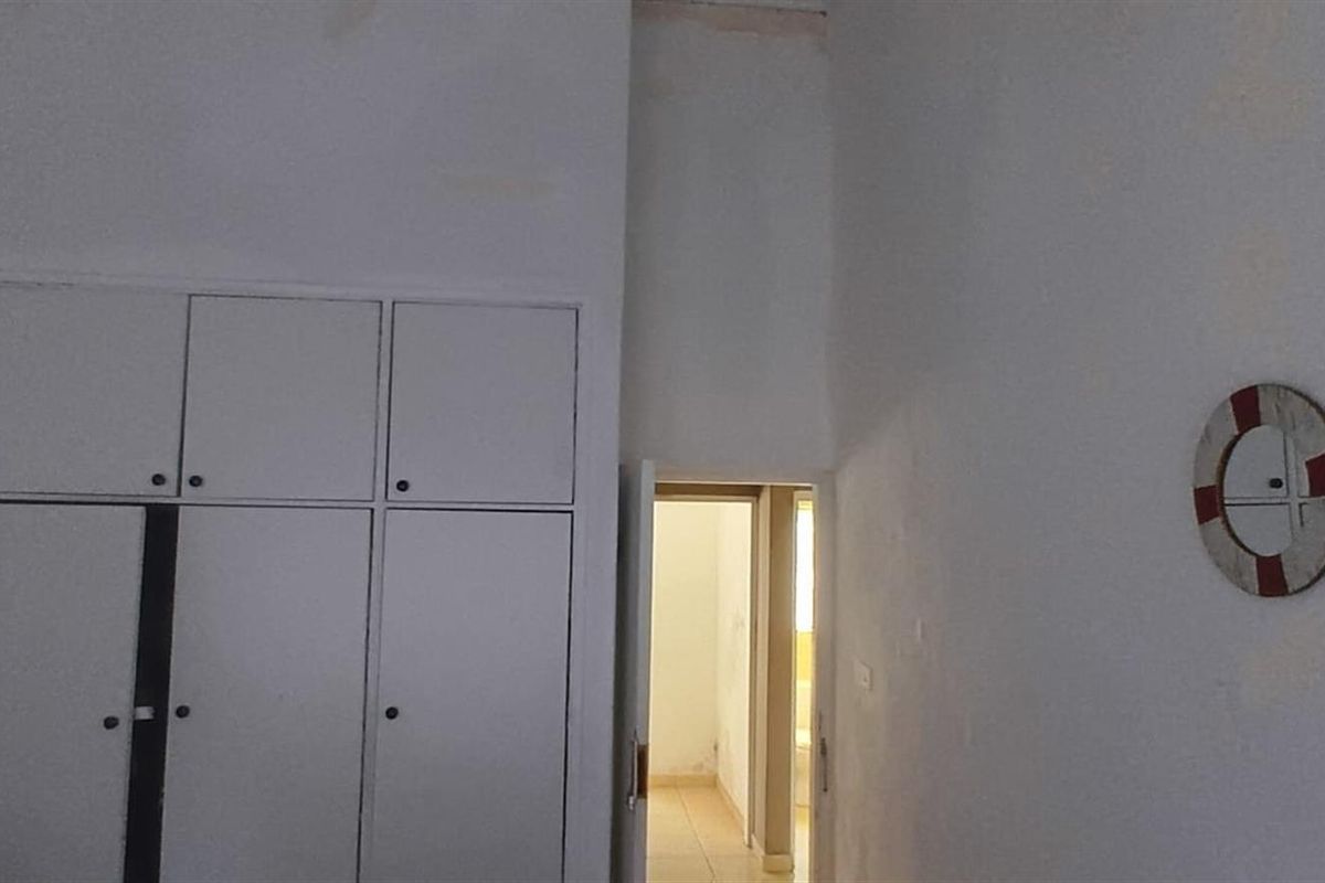 A bedroom interior featuring built-in cupboards and a doorway leading to an adjacent room, showing signs of wear on the ceiling.