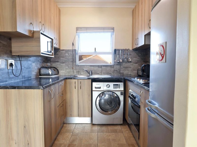 Compact kitchen featuring wood-finish cabinetry, stone-look backsplash, built-in oven, hob, and integrated washing machine.