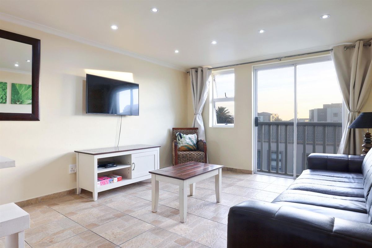 A bright living room featuring tiled flooring, recessed downlighting, and a sliding glass door providing access to a private balcony.