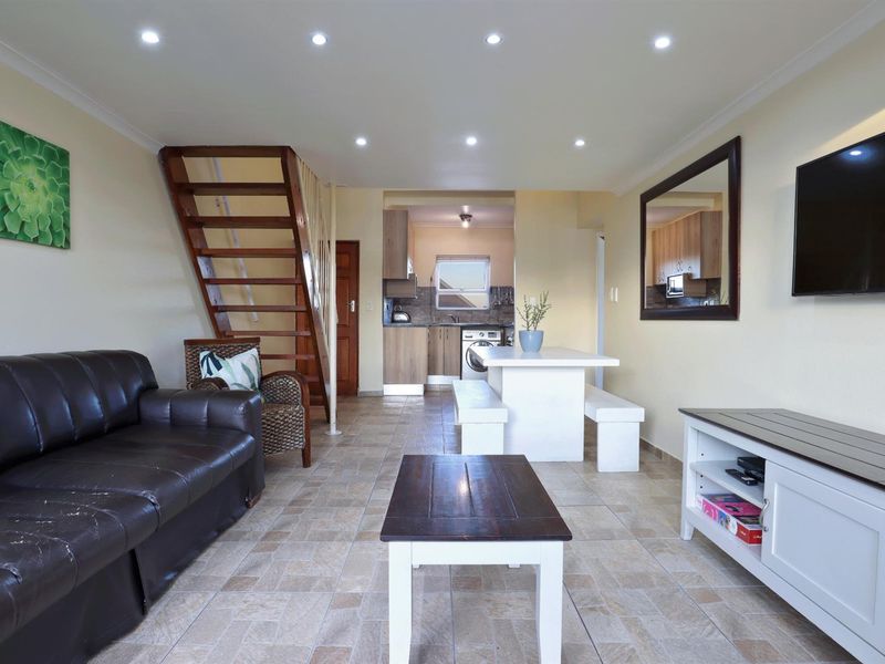 Open-plan living and dining area featuring tiled floors, recessed lighting, and an integrated kitchen space with a wooden staircase leading to the upper level.