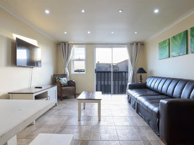 A bright living room featuring tiled flooring, recessed downlighting, and a sliding glass door providing access to a balcony.