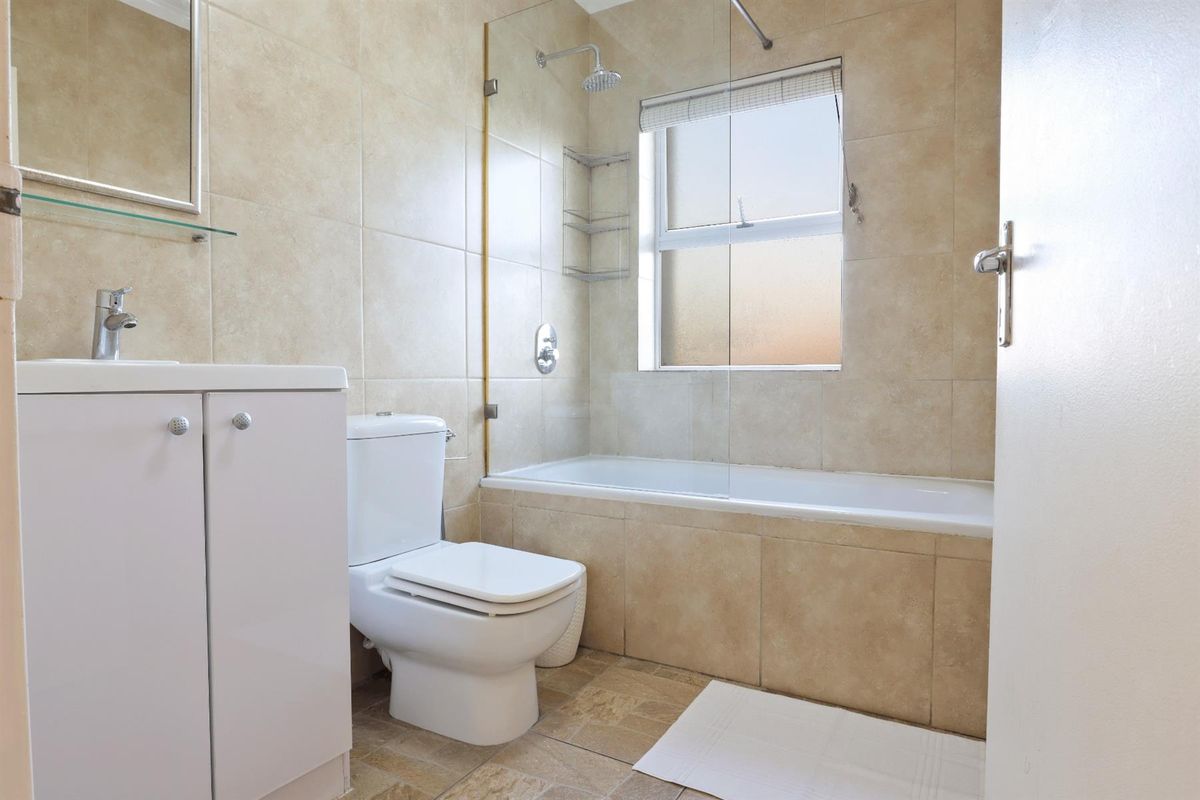 A clean, functional bathroom featuring a vanity cabinet, toilet, and a combined bathtub and shower with a glass screen and neutral wall tiling.