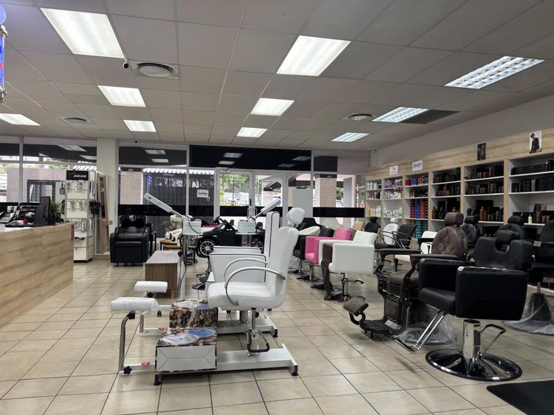 Spacious commercial salon interior featuring tiled flooring, suspended ceiling with recessed lighting, built-in product shelving, and a functional reception area.