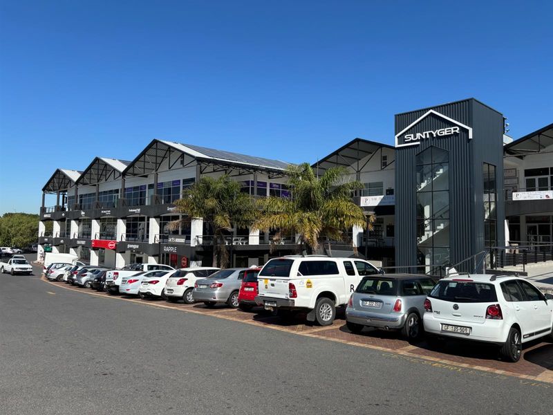 Front view of the Suntyger commercial complex featuring a multi-level facade, paved parking area, and modern architectural design with a prominent staircase tower.