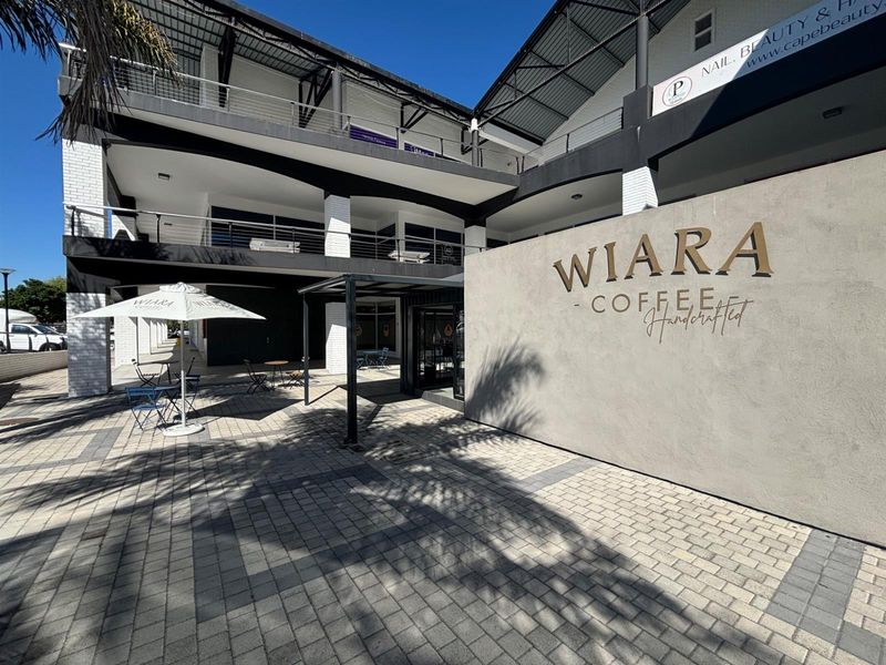 Front exterior view of a multi-level commercial building featuring a paved courtyard, covered walkways, and prominent signage for a coffee shop.