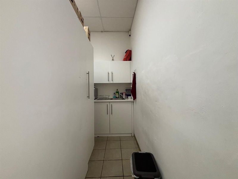 A compact scullery or kitchenette area featuring built-in white cabinetry, a sink, and tiled flooring, suitable for utility or staff use.