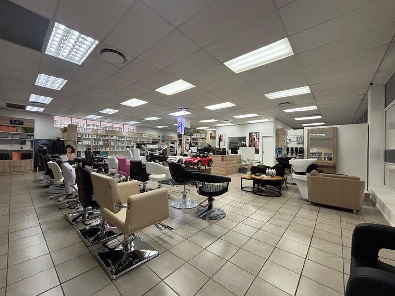 A well-maintained commercial salon space featuring tiled flooring, suspended ceilings with recessed lighting, built-in product shelving, and dedicated wash and styling stations.
