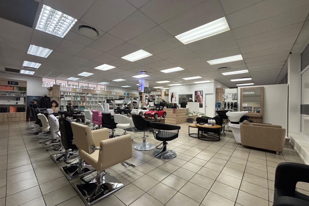 A well-maintained commercial salon space featuring tiled flooring, suspended ceilings with recessed lighting, built-in product shelving, and dedicated wash and styling stations.