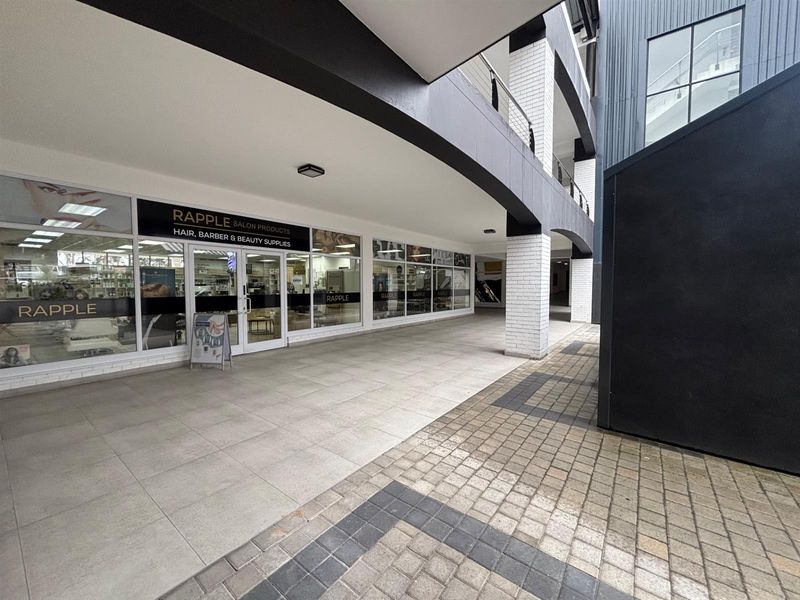 Commercial storefront entrance featuring a covered tiled walkway, glass facade, and modern brick architectural detailing in a well-maintained retail complex.