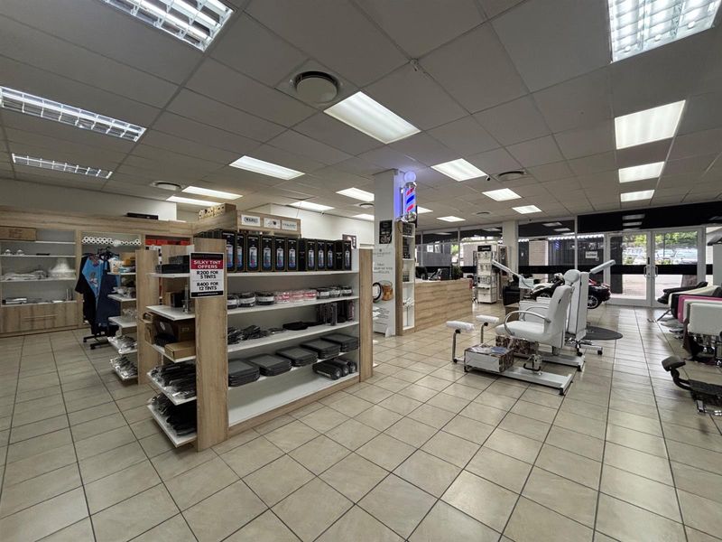 A well-maintained commercial salon space featuring tiled flooring, suspended ceilings with recessed lighting, built-in shelving, and a reception area.