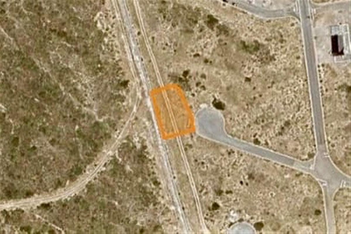 An aerial view of a vacant residential plot of land, highlighted with an orange boundary, situated within a developing neighborhood.