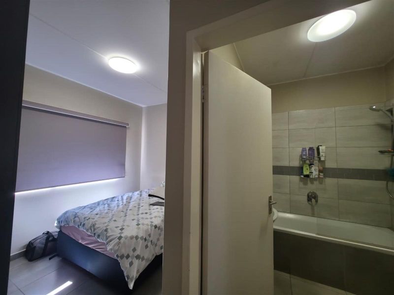 A view from a hallway looking into a bedroom and an adjacent bathroom featuring tiled walls and a bathtub.