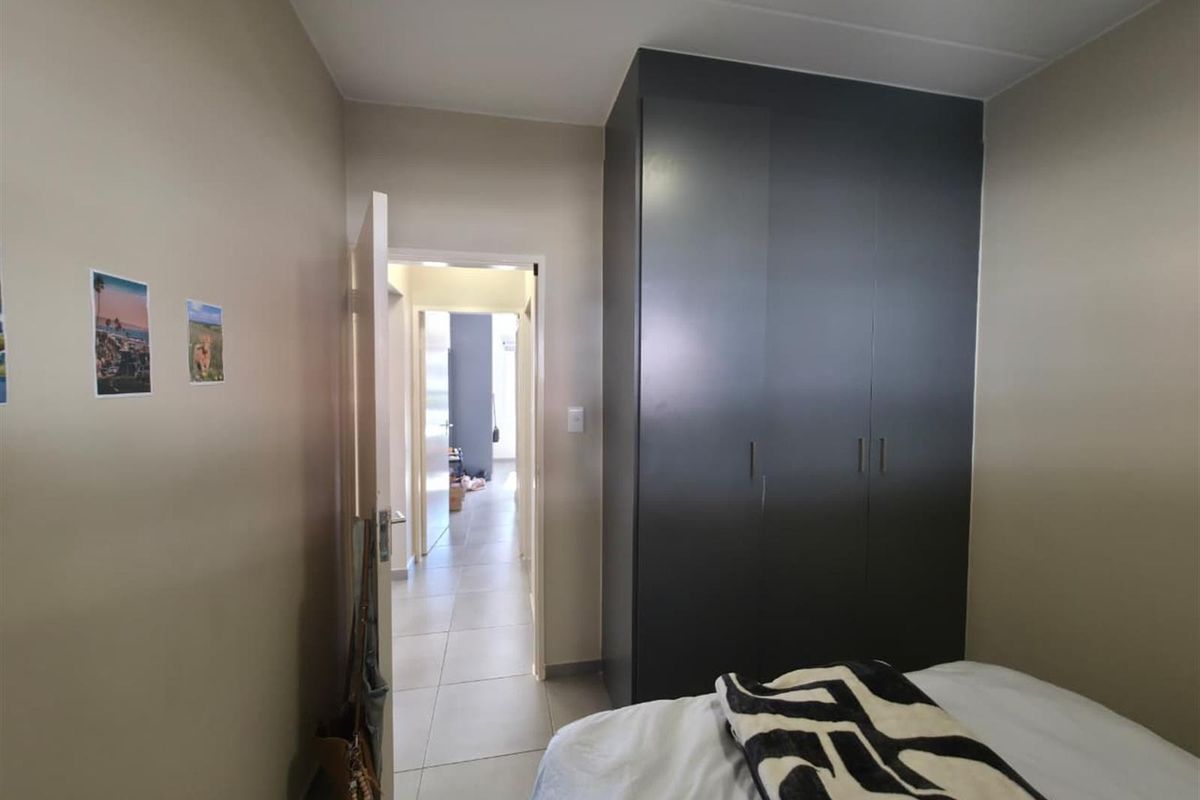 A bedroom featuring a dark built-in wardrobe and tiled flooring, with a view leading into the hallway.