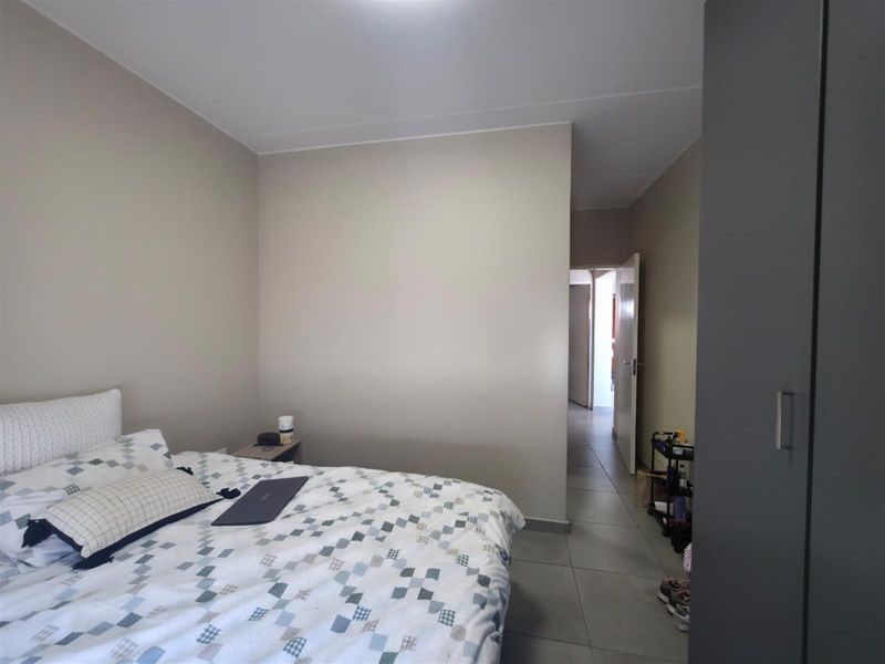 A bedroom featuring neutral wall tones, tiled flooring, and a built-in wardrobe, with an adjacent hallway visible.