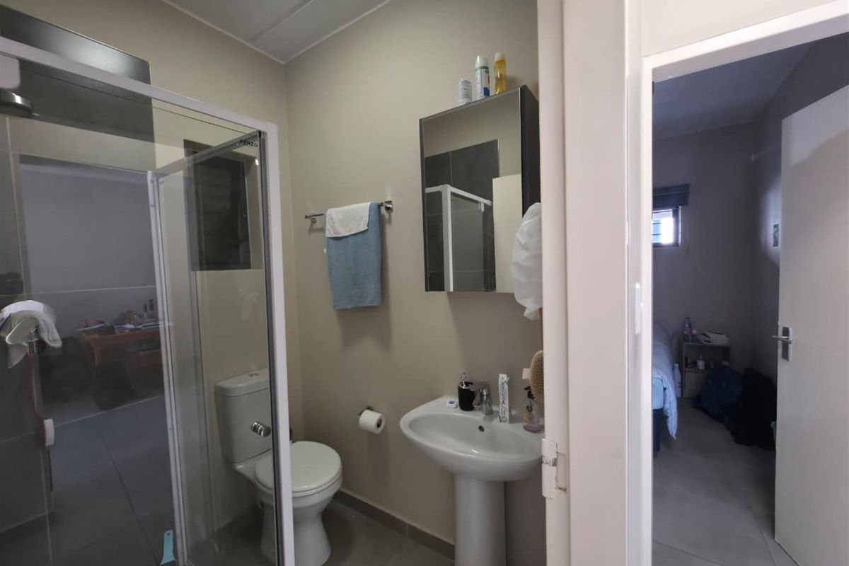 A functional bathroom featuring a pedestal basin, a glass-enclosed shower, and a toilet, with neutral wall tones and tiled flooring.