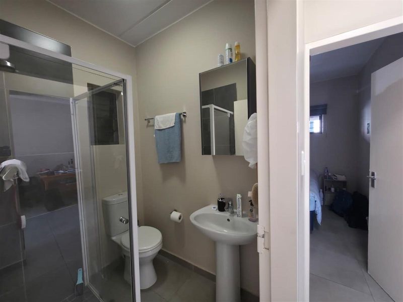 A functional bathroom featuring a pedestal basin, a glass-enclosed shower, and a toilet, with neutral wall tones and tiled flooring.