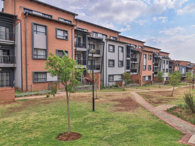 A view of the rear elevation of a modern apartment complex featuring brick and rendered facades, private balconies, and well-maintained communal garden areas.