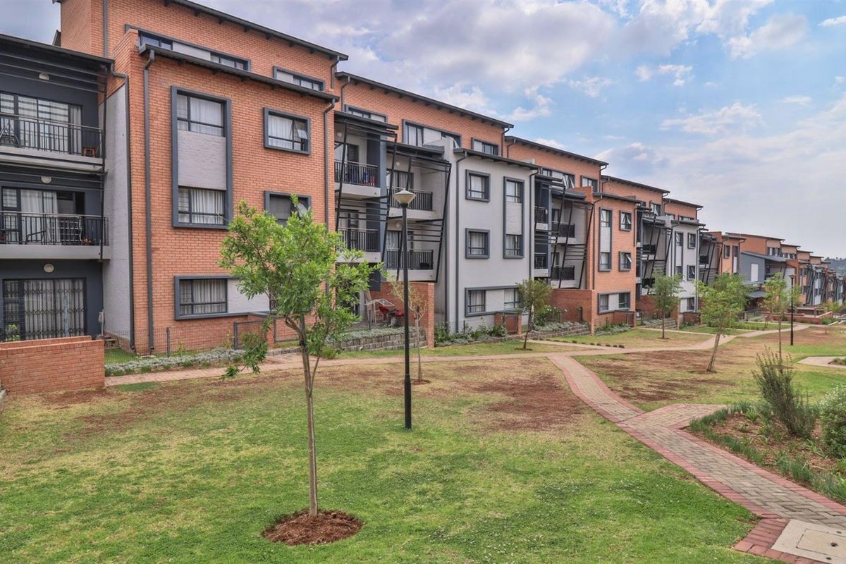 A view of the rear elevation of a modern apartment complex featuring brick and rendered facades, private balconies, and well-maintained communal garden areas.