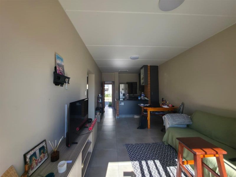 Open-plan living area featuring tiled flooring and a functional kitchen with a breakfast counter, leading towards an exterior entrance.