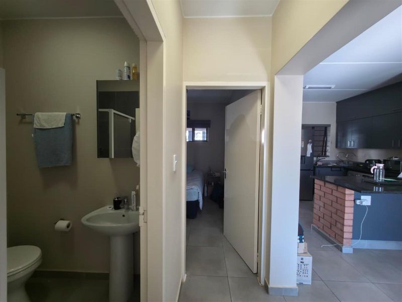 A view from the hallway looking into a bathroom, a bedroom, and an open-plan kitchen area with a brick breakfast bar.